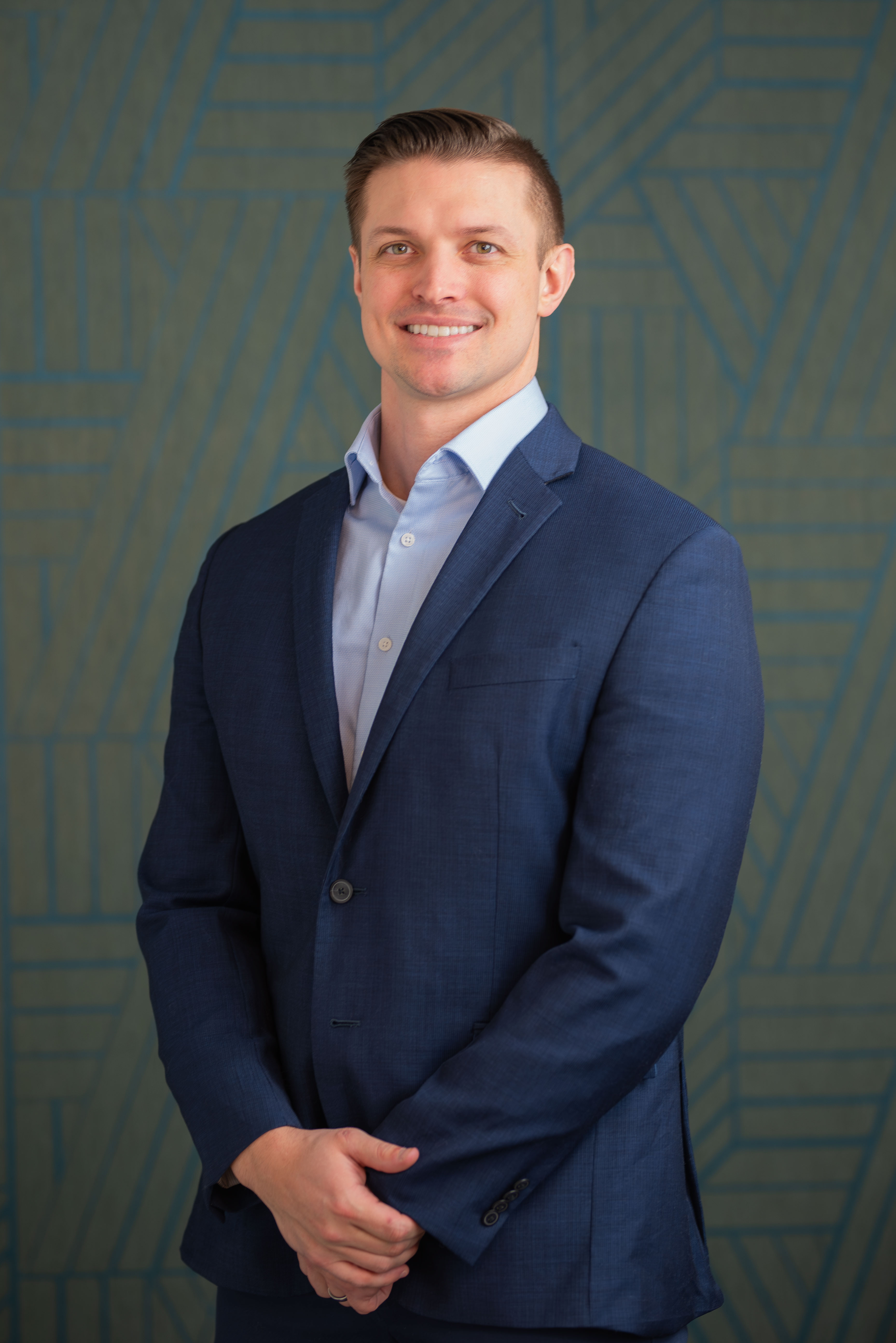 Smiling professional in navy blue suit against geometric patterned background