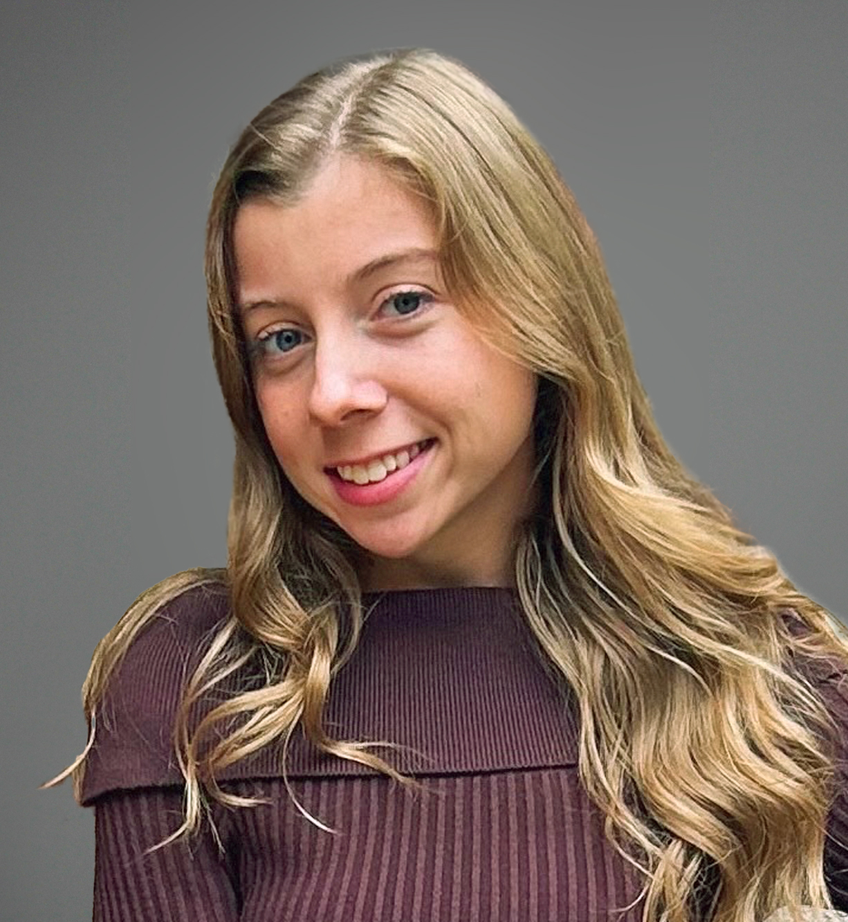 Smiling young woman with blonde wavy hair wearing a brown ribbed top Headshot