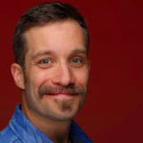 Smiling man with mustache in blue shirt against deep red background