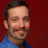 Smiling man with mustache in blue shirt against deep red background Headshot