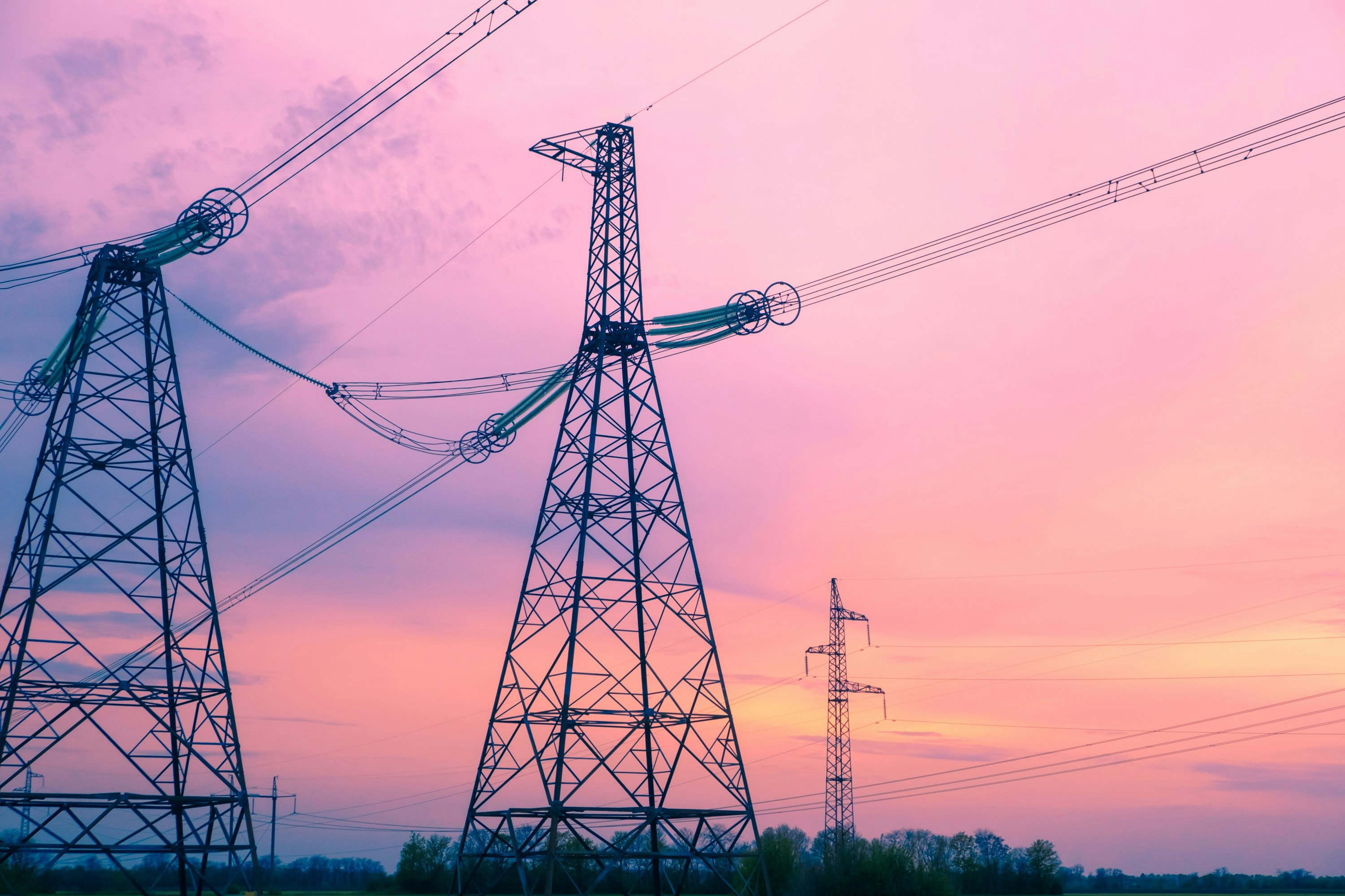 High-voltage electrical transmission towers silhouetted against a vibrant pink and orange sunset sky with clouds