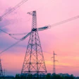 High-voltage electrical transmission towers silhouetted against a vibrant pink and orange sunset sky with clouds