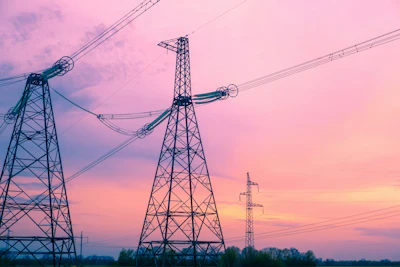 High-voltage electrical transmission towers silhouetted against a vibrant pink and orange sunset sky with clouds
