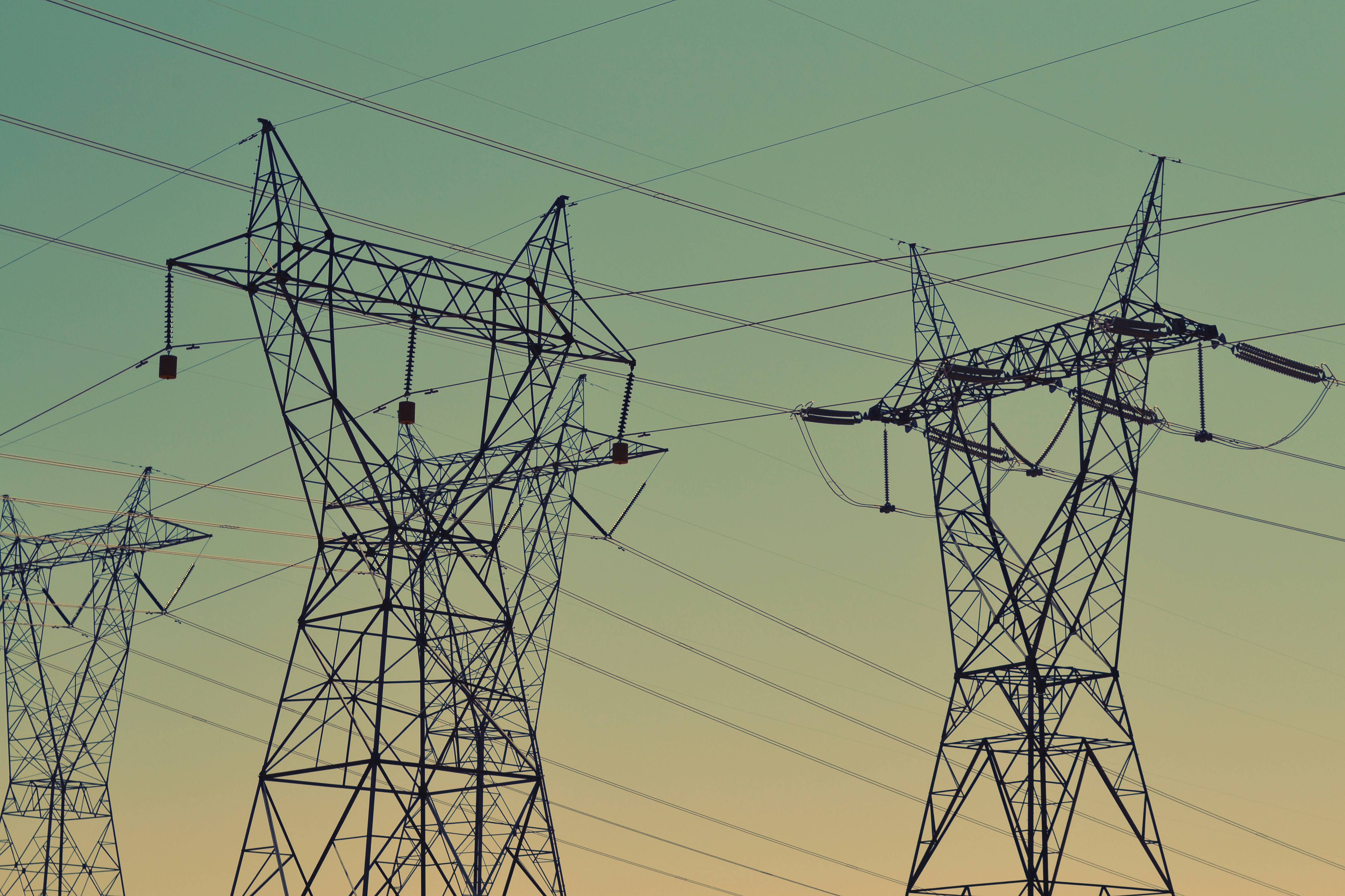 High-voltage electrical transmission towers silhouetted against a green and yellow gradient sky at dusk