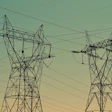 High-voltage electrical transmission towers silhouetted against a green and yellow gradient sky at dusk