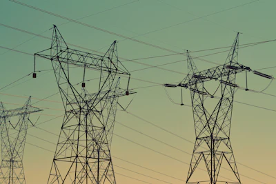 High-voltage electrical transmission towers silhouetted against a green and yellow gradient sky at dusk