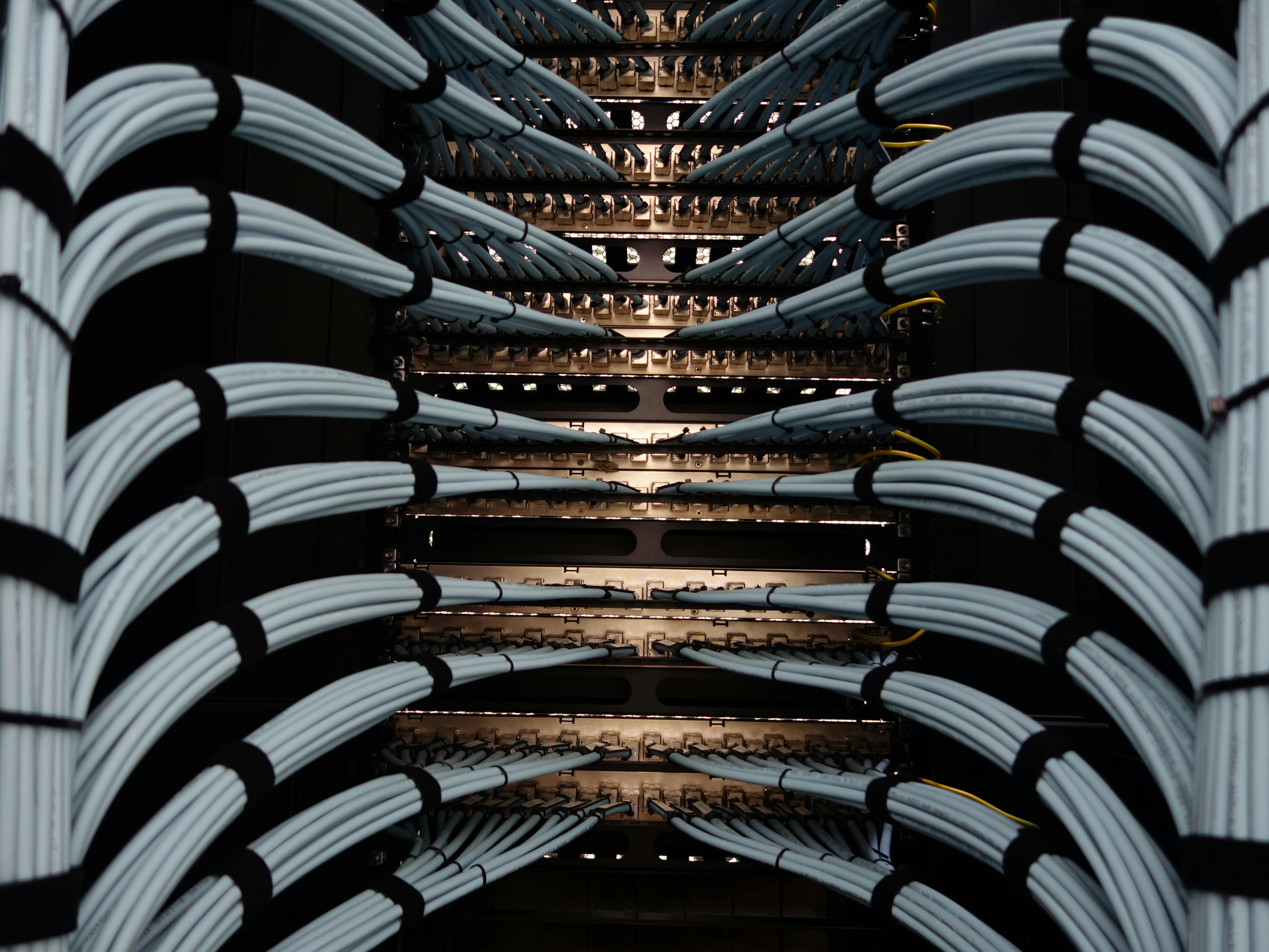 Network server rack with bundled white and black ethernet cables connected to illuminated patch panels in a data center