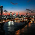 Williamsburg Bridge spanning the East River at dusk with Manhattan skyline illuminated against a gradient sunset sky