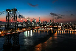 Williamsburg Bridge spanning the East River at dusk with Manhattan skyline illuminated against a gradient sunset sky