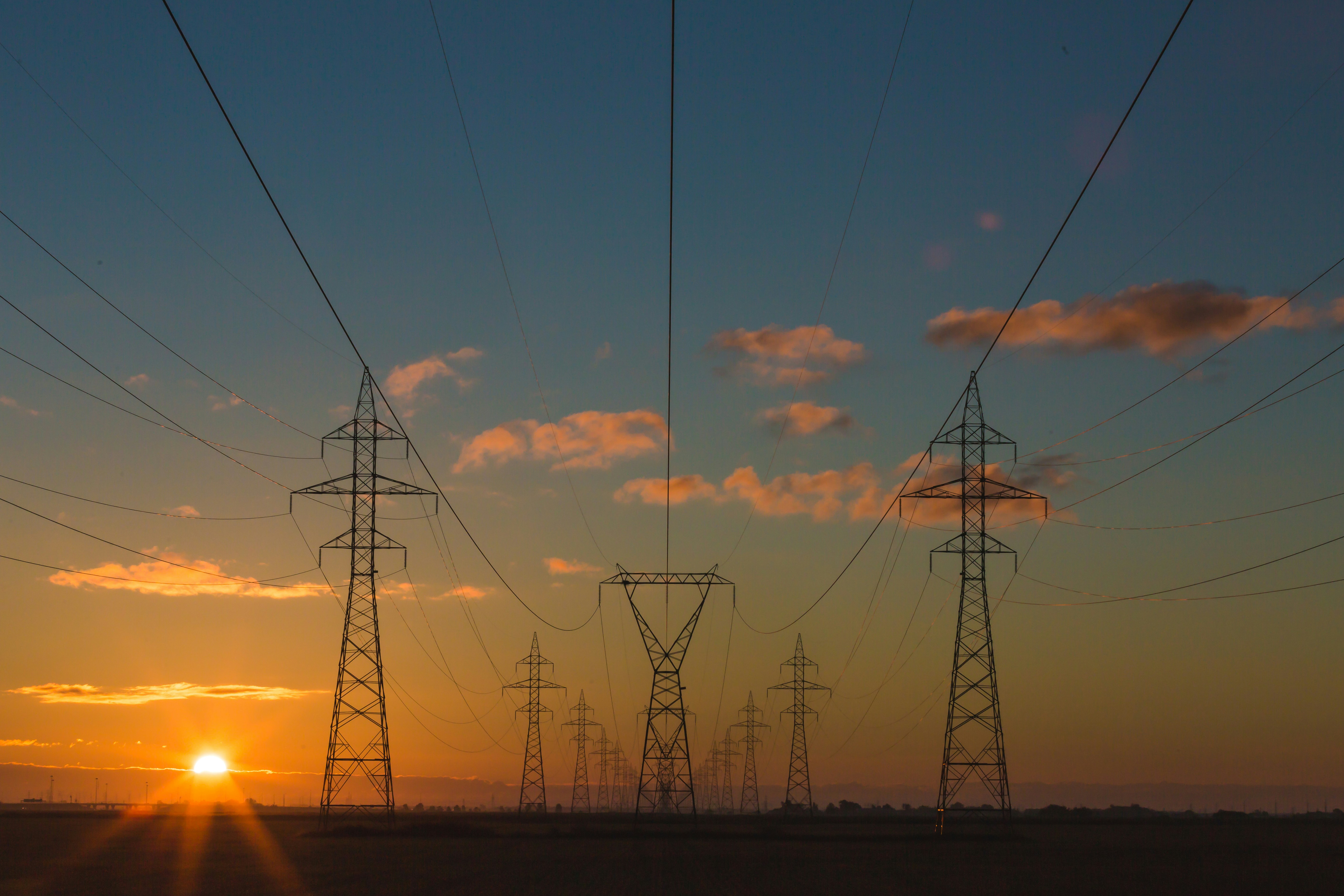 Electrical transmission towers silhouetted against a golden sunset with orange clouds