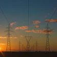 Electrical transmission towers silhouetted against a golden sunset with orange clouds