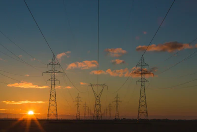 Electrical transmission towers silhouetted against a golden sunset with orange clouds