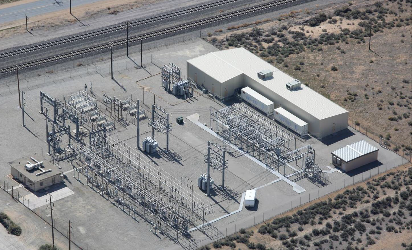Aerial view of electrical substation with transmission towers, concrete buildings, and equipment in desert landscape