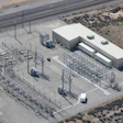 Aerial view of electrical substation with transmission towers, concrete buildings, and equipment in desert landscape