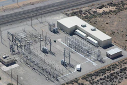Aerial view of electrical substation with transmission towers, concrete buildings, and equipment in desert landscape