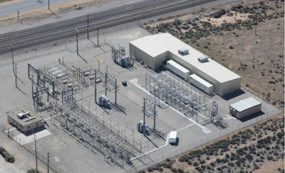 Aerial view of electrical substation with transmission towers, concrete buildings, and equipment in desert landscape