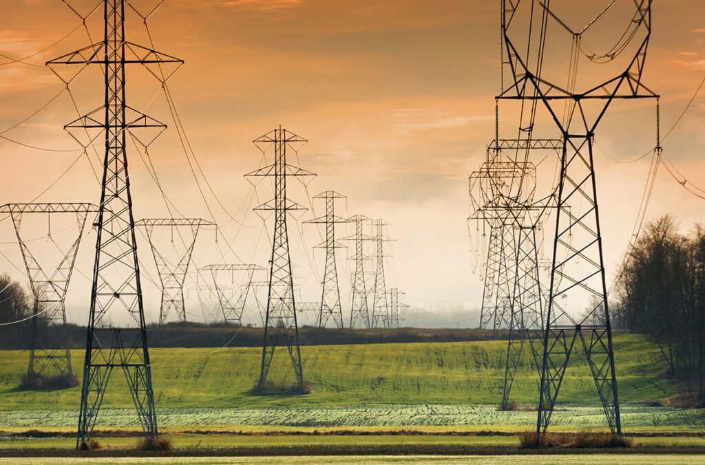High-voltage transmission towers stretching across a green field under golden sunset sky