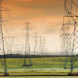High-voltage transmission towers stretching across a green field under golden sunset sky