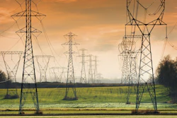 High-voltage transmission towers stretching across a green field under golden sunset sky