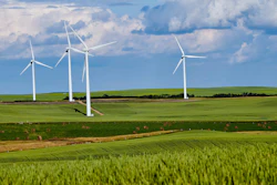 Wind turbines in green agricultural fields under blue sky with white clouds