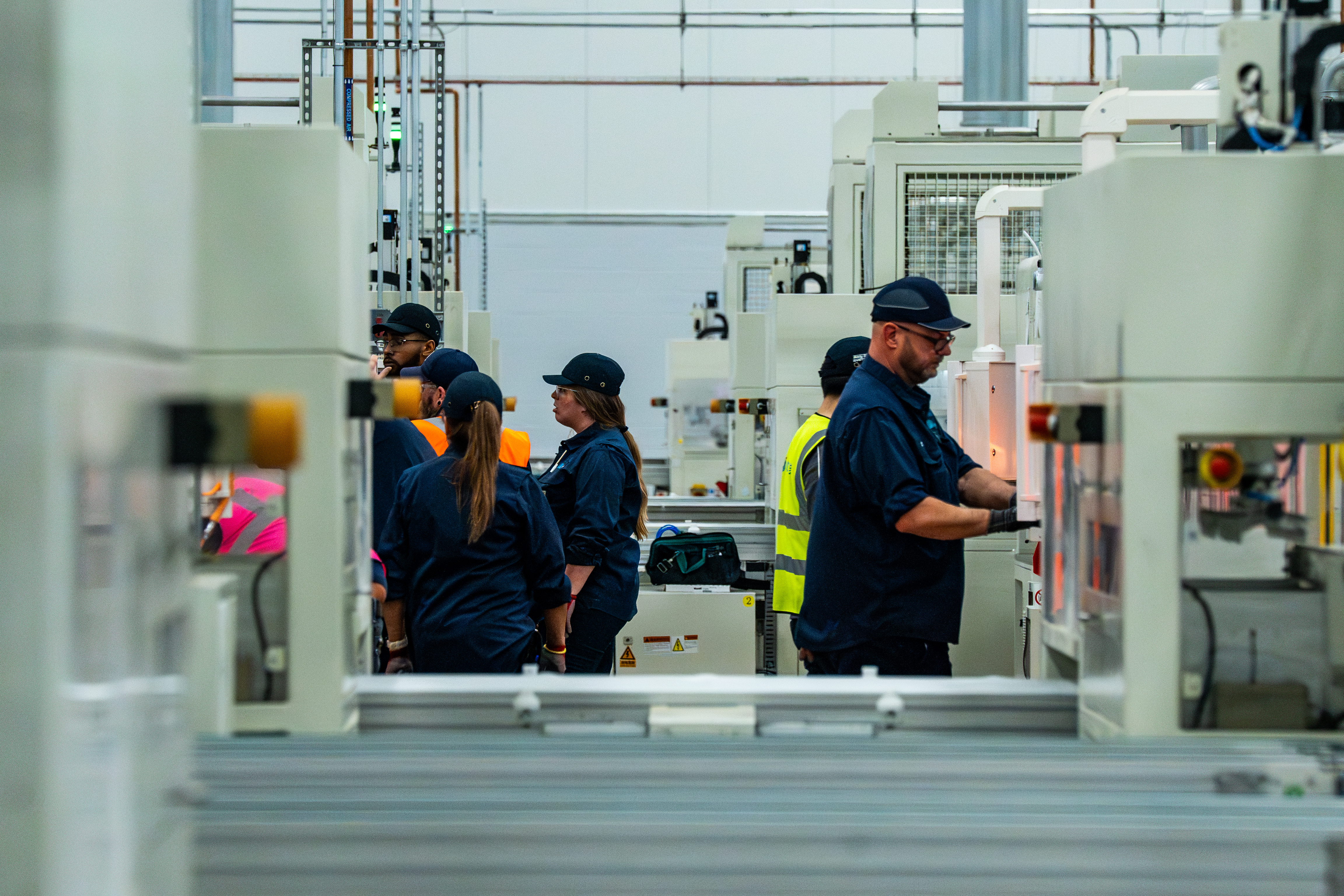 Factory workers in safety gear operating machinery on an industrial production floor
