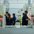 Factory workers in safety gear operating machinery on an industrial production floor