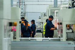 Factory workers in safety gear operating machinery on an industrial production floor
