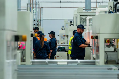 Factory workers in safety gear operating machinery on an industrial production floor