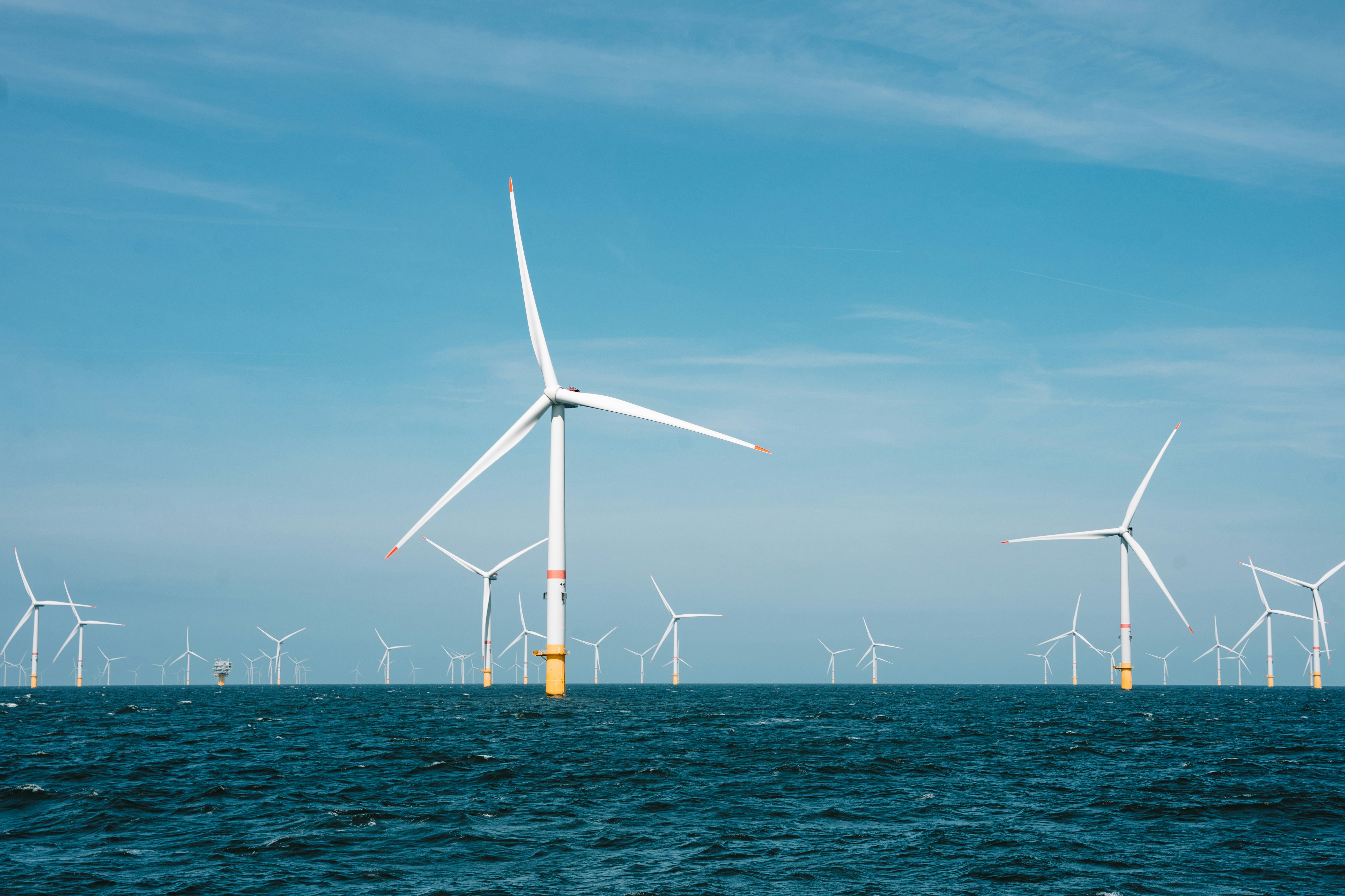 Offshore wind farm with multiple white turbines generating renewable energy in blue ocean waters under clear sky