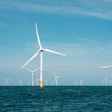 Offshore wind farm with multiple white turbines generating renewable energy in blue ocean waters under clear sky