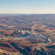 Aerial view of industrial manufacturing complex with tall smokestacks surrounded by autumn forests and agricultural fields