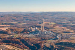 Aerial view of industrial manufacturing complex with tall smokestacks surrounded by autumn forests and agricultural fields