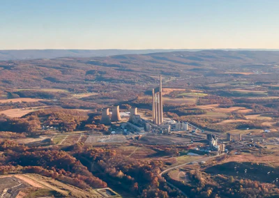 Aerial view of industrial manufacturing complex with tall smokestacks surrounded by autumn forests and agricultural fields