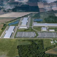 Aerial view of industrial manufacturing facility with warehouses, solar panels, and parking areas surrounded by agricultural fields