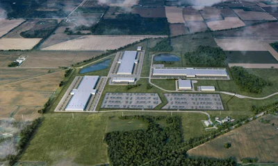 Aerial view of industrial manufacturing facility with warehouses, solar panels, and parking areas surrounded by agricultural fields