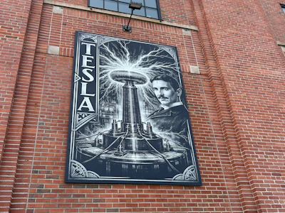 Historical mural of Nikola Tesla with his wireless transmission coil on brick building facade