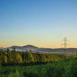 Power transmission towers spanning across forested valley at sunset with mountains in background